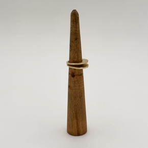 A gold ring with a textured, organic wavy band displayed on a wooden ring cone against a plain light gray background.