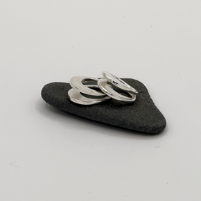 Polished silver rings stacked on a small dark gray stone, photographed on a plain light gray background.