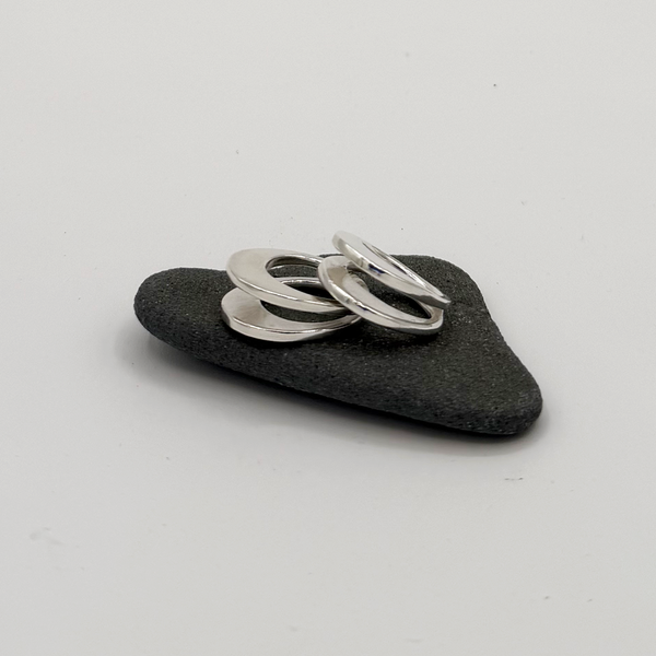 Polished silver rings stacked on a small dark gray stone, photographed on a plain light gray background.