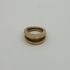A gold-colored ring with a textured outer band and a smooth inner channel, photographed on a plain light gray background.