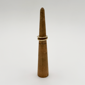 A gold ring displayed on a wooden cone ring stand against a plain light gray background.